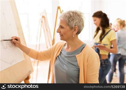 art school, creativity and people concept - happy senior woman artist with easel and pencil drawing picture at studio. woman artist with pencil drawing at art school