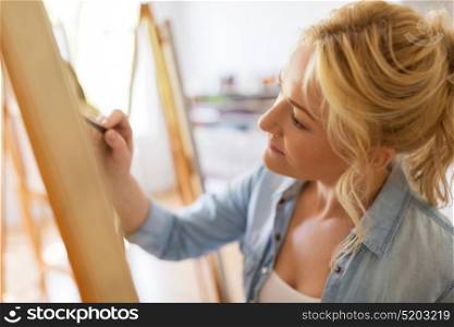 art school, creativity and people concept - happy woman artist with easel and pencil drawing picture at studio. woman artist with pencil drawing at art school