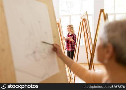 art school, creativity and people concept - student girl or artist with easel, palette and paint brush painting still life picture at studio. student girl with easel painting at art school
