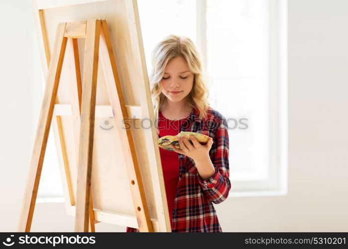 art school, creativity and people concept - student girl or artist with easel and palette painting at studio. student girl with easel painting at art school