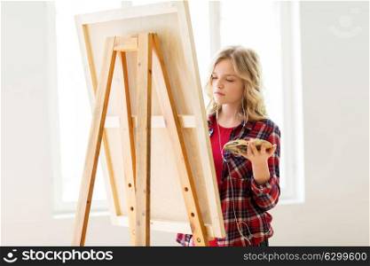 art school, creativity and people concept - student girl or artist with earphones, easel and palette painting at studio. student girl with easel painting at art school