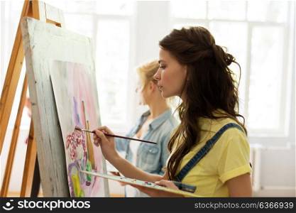 art school, creativity and people concept - woman with easel, palette and brush painting at studio. woman with easel painting at art school studio