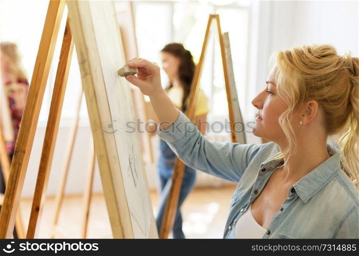 art school, creativity and people concept - woman with eraser and easel drawing at studio. woman with easel drawing at art school studio