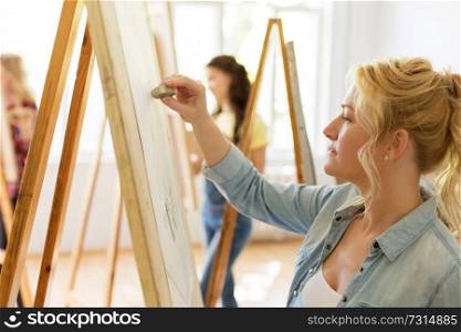 art school, creativity and people concept - woman with eraser and easel drawing at studio. woman with easel drawing at art school studio