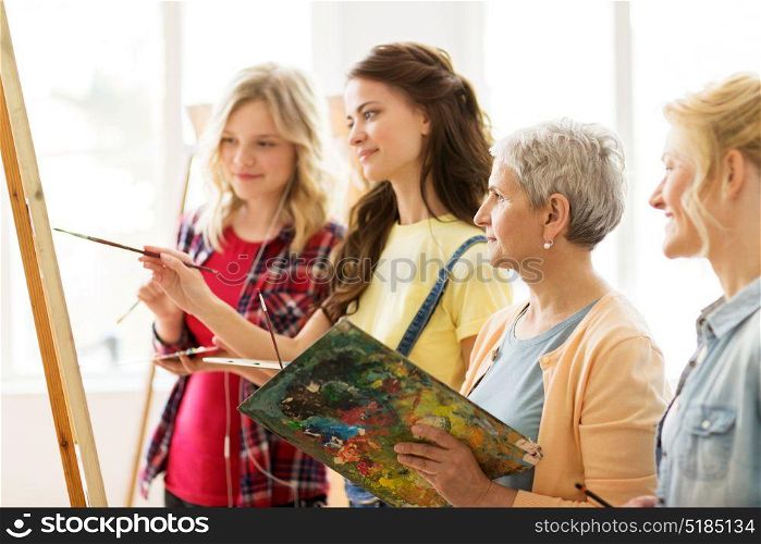 art school, creativity and people concept - women artists with easel, paint brushes and palettes painting at studio. women with easel and palettes at art school