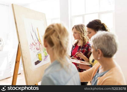 art school, creativity and people concept - women artists with easel, paint brushes and palettes painting at studio. women with easel and palettes at art school