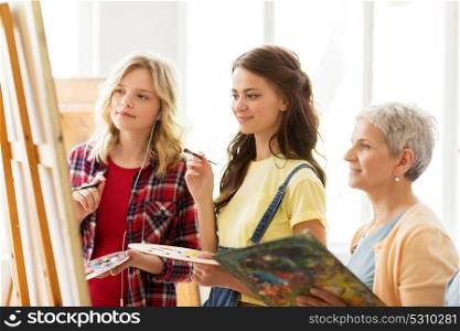 art school, creativity and people concept - women artists with easel, paint brushes and palettes painting at studio. women with easel and palettes at art school