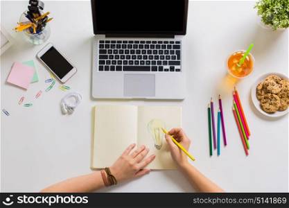art, startup and freelance concept - woman hands with pencil drawing light bulb in notebook at home office. woman hands drawing in notebook at home office