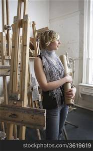 Art student standing, holding rolled-up artwork, in studio
