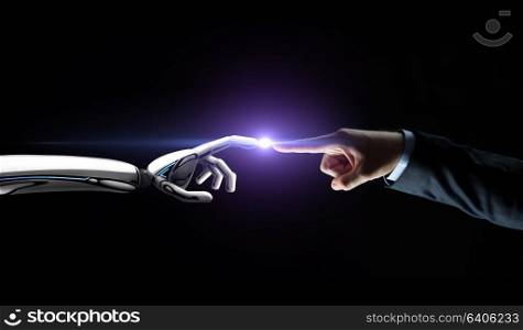 artificial intelligence, future technology and communication concept - robot and human hand connecting fingers on black background with flare. robot and human hand connecting fingers