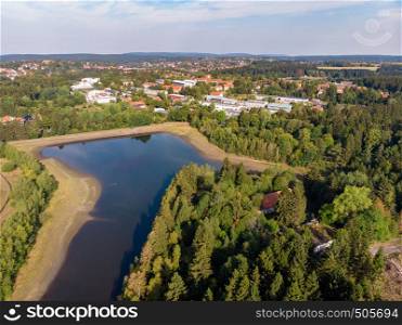 Artificial pond in the Harz Mountains with a neighbouring meadow and a small town in the background, aerial photo with the drone