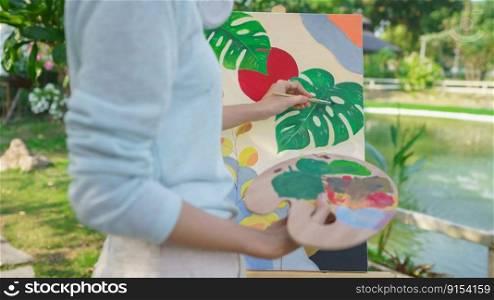 Artist concept, Female artist holding color palette and painting picture on canvas in the garden.