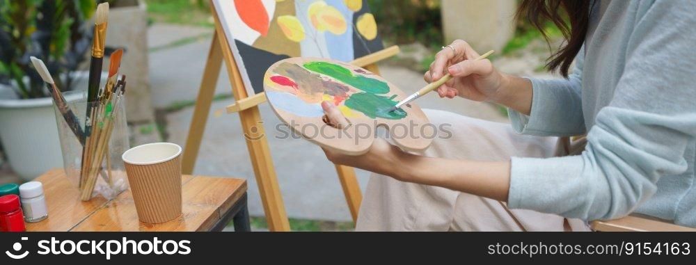 Artist concept, Female artist use brush to mix color on palette for painting on canvas in garden.
