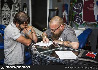 Artist drawing up tattoo ideas with a client