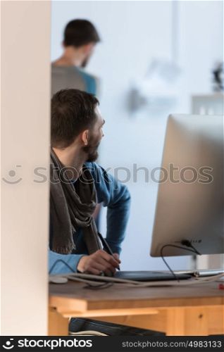 Artist or designer drawing something on graphic tablet at the office with colleague on background