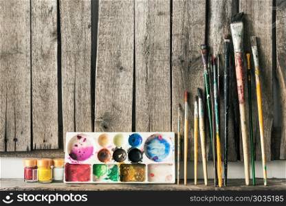 Artist paint brushes and palette on wooden background.