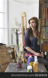Artist sitting at easel, contemplating, in studio