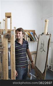Artist standing by charcoal portrait in studio