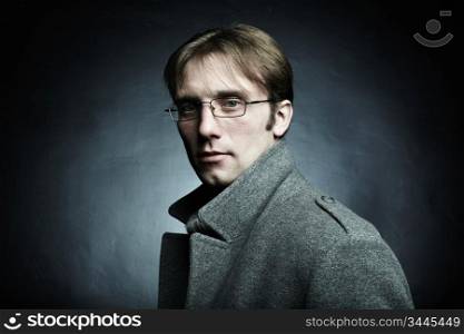 Artistic dark portrait of the young beautiful man in a gray coat