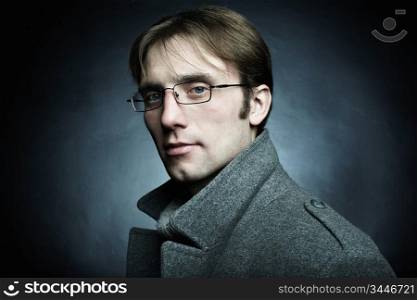 Artistic dark portrait of the young beautiful man in a gray coat