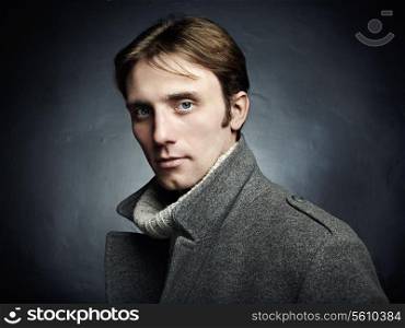 Artistic dark portrait of the young beautiful man in a gray coat. Close up