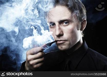 Artistic dark portrait of the young beautiful man. The young man smokes a tube