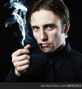 Artistic dark portrait of the young beautiful man. The young man smokes a tube. Close up