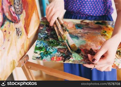 artists brushes and oil paints on wooden palette. macro artist&rsquo;s palette, texture mixed oil paints in different colors and saturation. palette with paintbrush and palette-knife in artist&rsquo;s hands. The girl artist holding a palette with oil paints