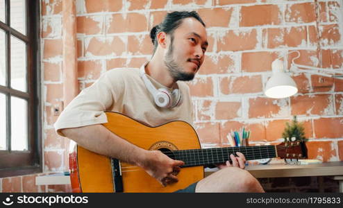 Artists producing music in their home sound studio, Asian man playing guitar and singing in living room at home. Lifestyle man relax in morning at home concept.