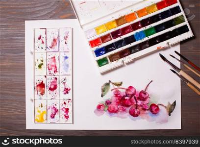 Artwork, watercolor painting cherries with drawing tools on a wooden table. Watercolor painting cherries