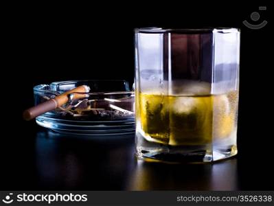 ashtray full of butts and glass of whiskey on black background