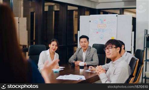 Asia businessmen and businesswomen meeting brainstorming ideas conducting business presentation project colleagues working together plan success strategy enjoy teamwork in small modern night office.
