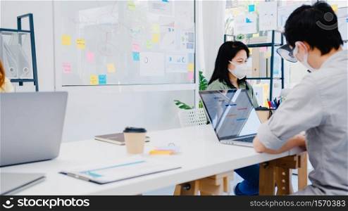 Asia businesspeople entrepreneur wearing medical face mask for social distancing in new normal situation for virus prevention while using laptop back at work in office. Lifestyle after corona virus.