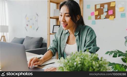 Asia businesswoman using laptop talk to colleagues about plan in video call while smart working from home at living room. Self-isolation, social distancing, quarantine for corona virus prevention.