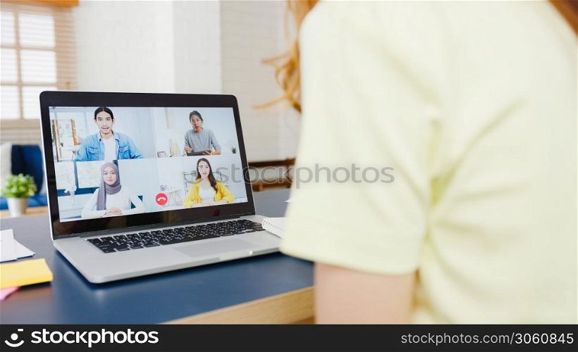 Asia businesswoman using laptop talk to colleagues about plan in video call meeting while working from home at living room. Self-isolation, social distancing, quarantine for corona virus prevention.
