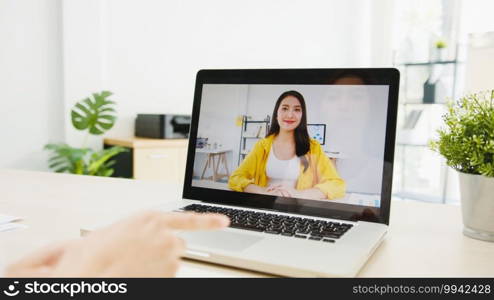 Asia businesswoman using laptop talk to colleagues about plan in video call meeting while working from home at living room. Self-isolation, social distancing, quarantine for corona virus prevention.