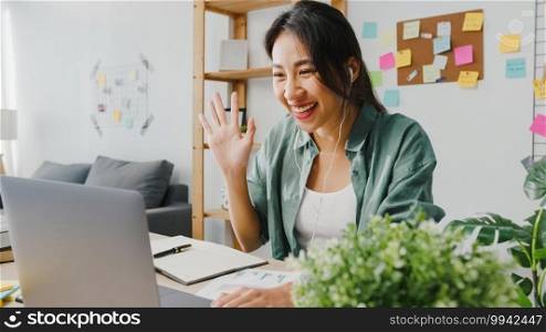 Asia businesswoman using laptop talk to colleagues about plan in video call while smart working from home at living room. Self-isolation, social distancing, quarantine for corona virus prevention.