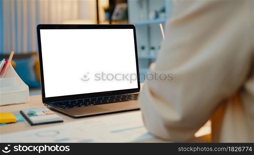 Asia businesswoman using laptop with blank white screen mock up display for advertising text talk to colleagues about plan in video call meeting at living room at house. Working overload at night.
