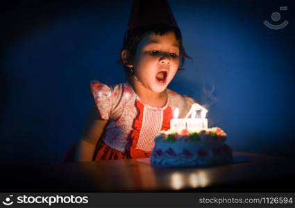 Asia child blowing out candles on birthday cake / Portrait of little pretty girl Happy Birthday Party at night