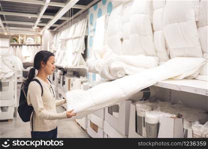 asia customer woman chooses bed linen and blanket in the supermarket mall store. She is examining mattress to pay.