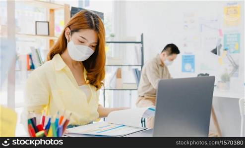 Asia female wear face mask for social distancing in new normal situation for virus prevention while using laptop and separated by acrylic partition stand in office. Life and work after corona virus.