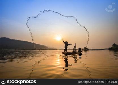 Asia fisherman net using on wooden boat casting net sunset or sunrise in the Mekong river / Silhouette fisherman boat with mountain background people life on countryside