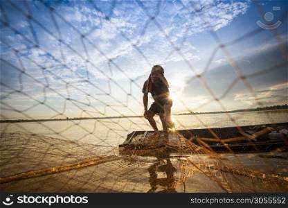 Asia fisherman net using on wooden boat casting net sunset or sunrise in the river - Silhouette fisherman boat with background life person countryside