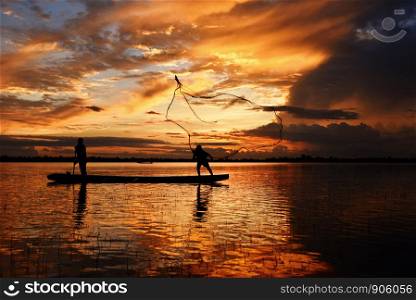 Asia fisherman net using on wooden boat casting net sunset or sunrise in the Mekong river - Silhouette fisherman boat with mountain background life person countryside