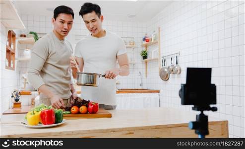 Asia gay couple blogger vlogger and online influencer recording video content on healthy food in kitchen at home. Young LGBT men talk happy relax rest together spend romantic time at house in morning.