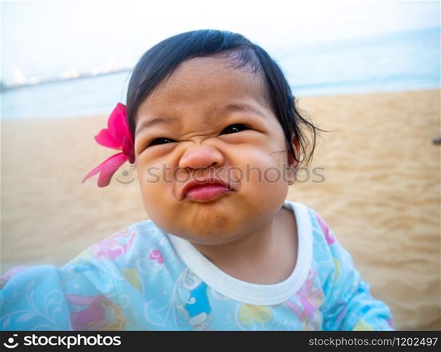 asia little girl making funny face and red flowers in her ear. Her sitting on the beach and looking happy