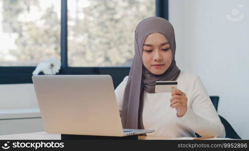 Asia muslim lady using laptop, credit card buy and purchase e-commerce internet in office. Stay at home, online shopping, self isolation, social distancing, quarantine for coronavirus prevention.