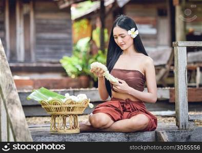 Asia woman drama style dress Sitting on old thai house / Portrait of beautiful young girl smiling traditional costume wearing with thai jasmine garland in hand