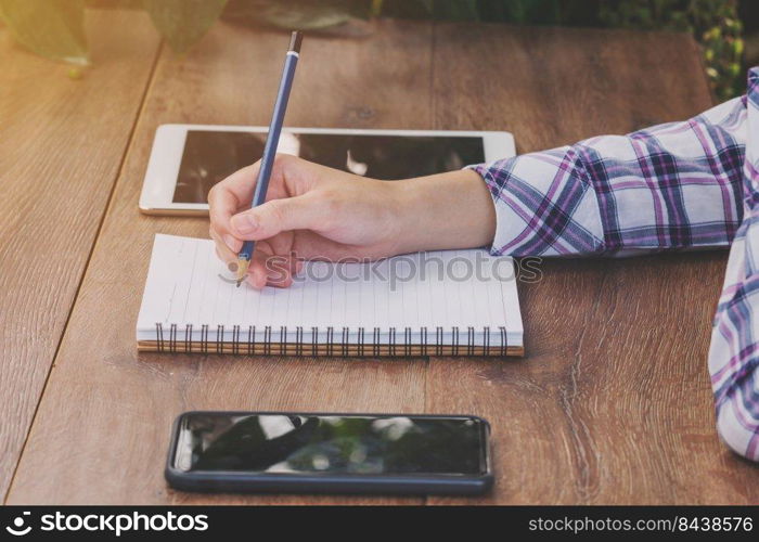 Asia woman hand writing notebook on wood table in coffee shop.