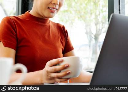 Asia woman hold cup of coffee while typing on laptop keyboard. Woman working at office with coffee